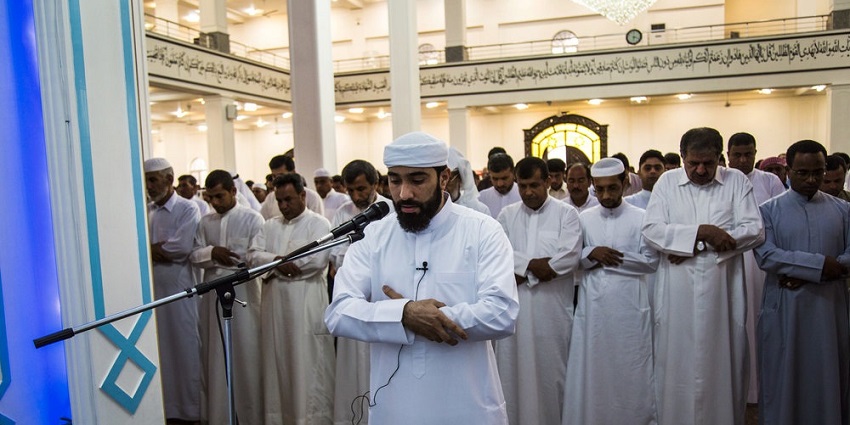 Imam leads the believers in prayer in a sunlit mosque during a religious holiday.