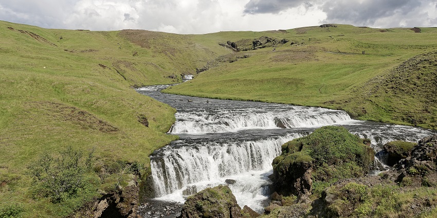 Waterfall flowing through hilly terrain with forested slopes and open landscapes around