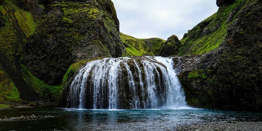 Waterfall flows through green rocky cliffs in a forest, perfect for nature lovers and things to do in Kazbegi.