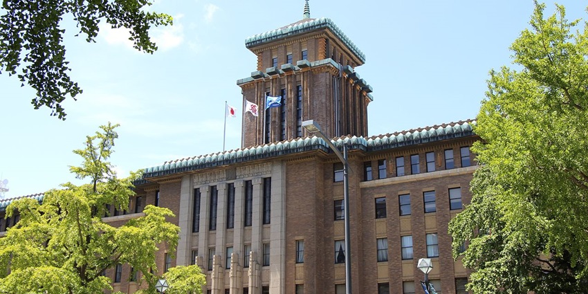 Historic Yokohama City Hall building with traditional Japanese architectural elements, surrounded by green trees and flags.