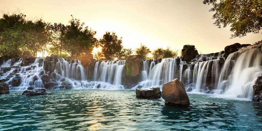 A wide curtain of water tumbling over a forested cliff into a serene turquoise pool