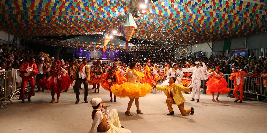 People dressed in vibrant costumes performing in the middle under colourful decorations