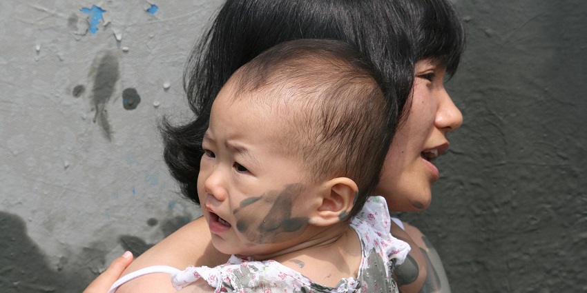 A woman holding a baby with slight mud on the baby’s cheeks, their hand and clothes