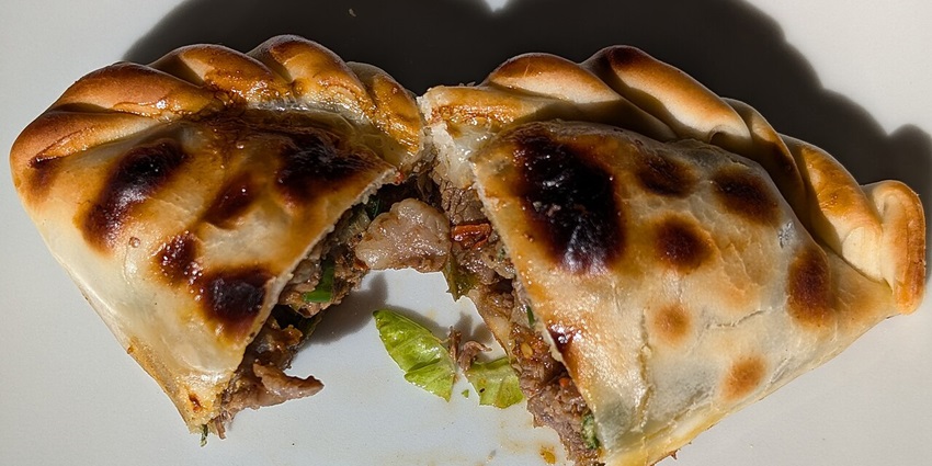 Open empanada showcasing a golden-brown crust filled with spiced beef, and onions.