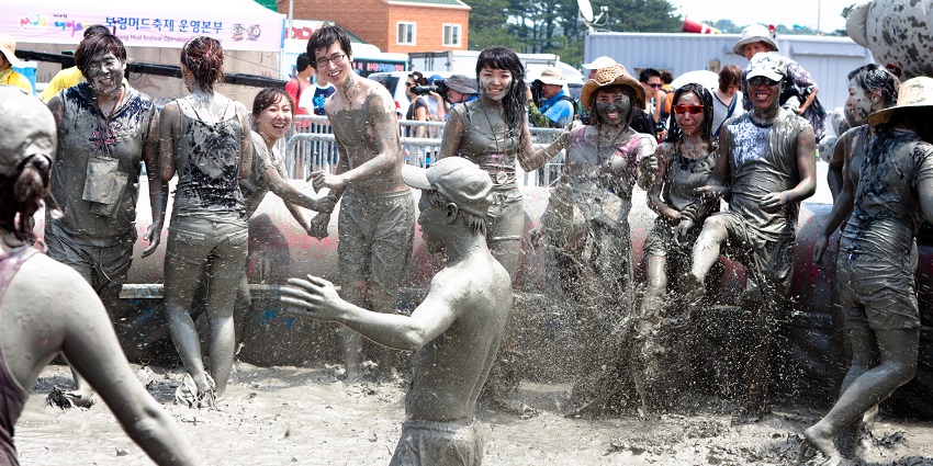 People covered in mud splashing mud in the pit, smiling and enjoying the festival