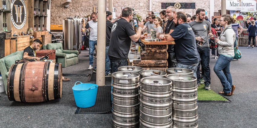 People standing in the brewery stalls in a fair with large barrels of wood and steel