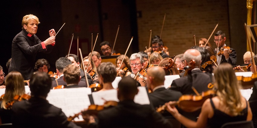 A person standing and guiding the group of people playing different instruments