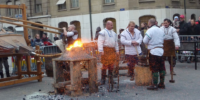 Men in traditional attire demonstrate metalworking with fire during Fête de l'Escalade.