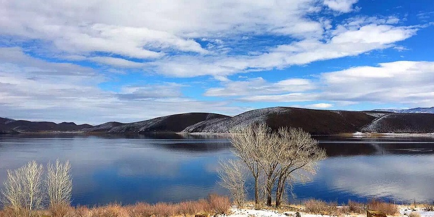 Bridgeport Reservoir with snow-capped mountains in the background and white snowy clouds