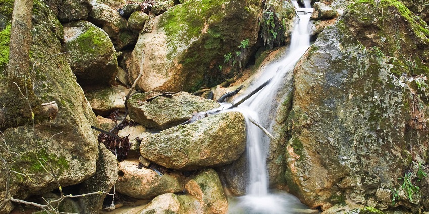 A waterfall cascading into a deep natural pool surrounded by steep rocky cliffs and moss.