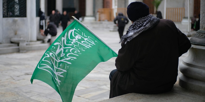 A man wearing traditional clothing with the Saudi Arabia flag in his right hand