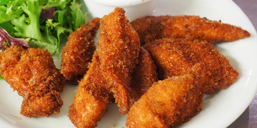 Tray of crispy fried chicken wings glazed in sticky barbecue sauce, a favorite street food in London.