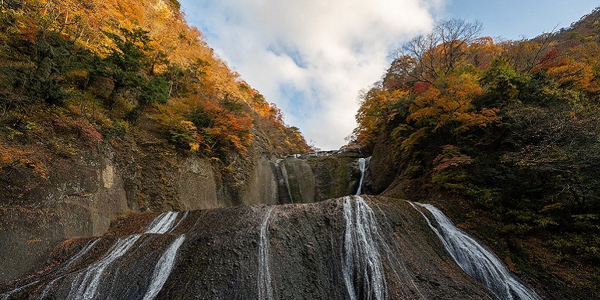 Fukuroda waterfall in Japan cascades over massive rocks, surrounded by colourful trees
