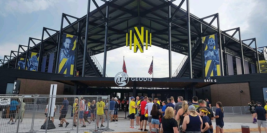 Gate of Geodis Park with people entering the stadium, American flags and multiple signages