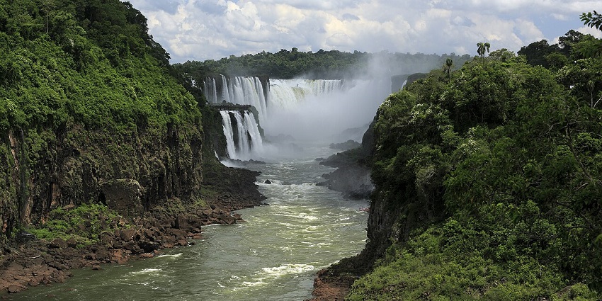 Scenic view of Garganta del Diablo waterfall with mist, lush greenery and cloudy sky.