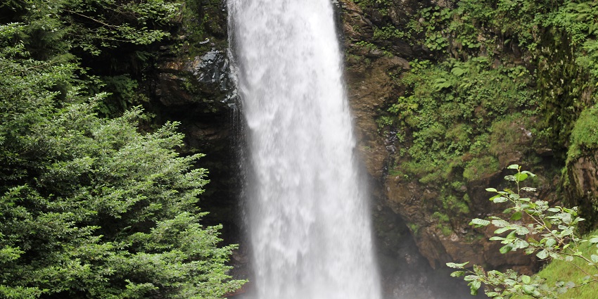 Waterfall flowing into the water body surrounded by green rocky cliffs under strong pressure.