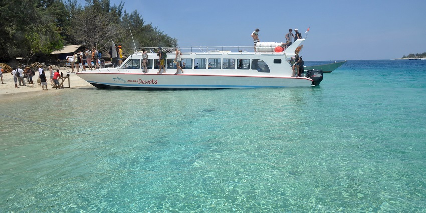 Passenger boats float on clear waters with the Gili Islands’ coastline visible under sunny skies.