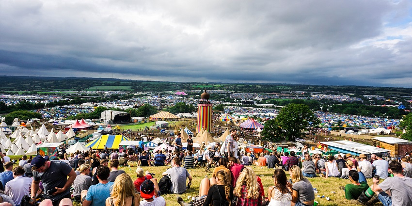 People sitting on the ground, overlooking multi-coloured tents, stalls and an open stage