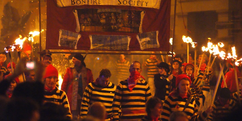 A procession of people dressed in red and black striped t-shirts holding torches and flags