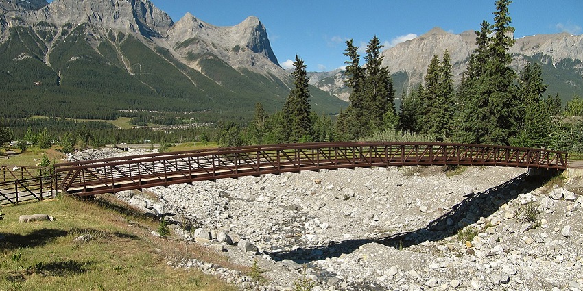 A wooden bridge built across a dry river bounded by breathtaking mountains on a pleasant day.