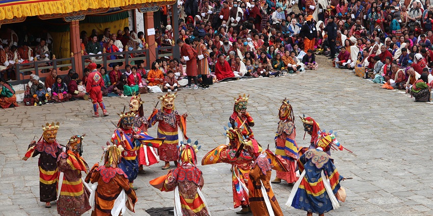 View of people in traditional clothes and masks performing a circular folk dance of Bhutan.
