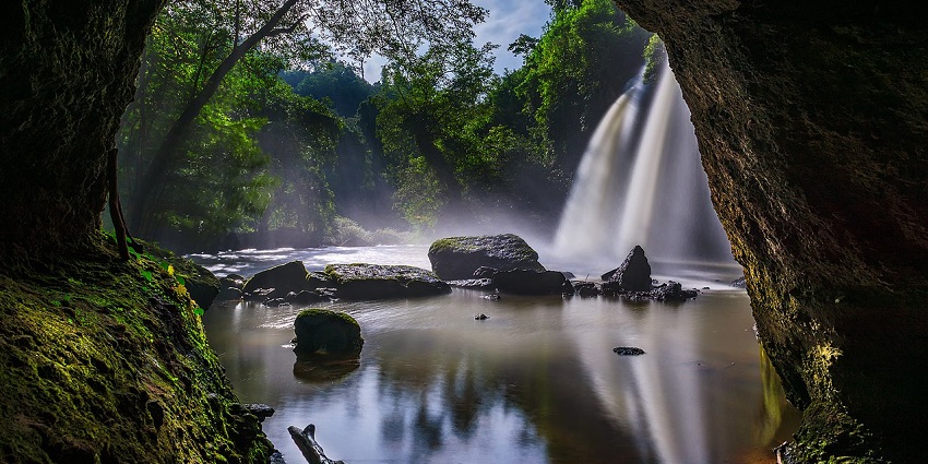 Calm waters reflect the chaotic drop of Haew Suwat Waterfall as seen from a nearby cave.