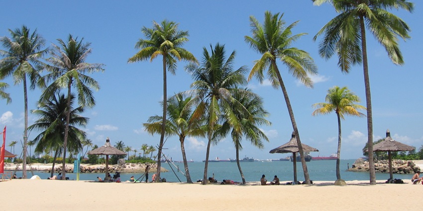 A peaceful panoramic view of Siloso Beach on Sentosa Island, Singapore, captured in daylight with soft blue skies.