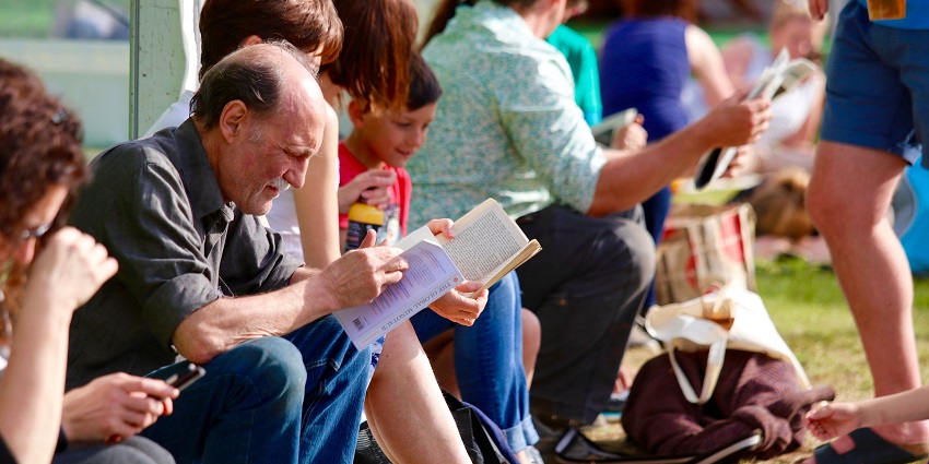 A group of people gathered together, reading books, talking and enjoying drinks
