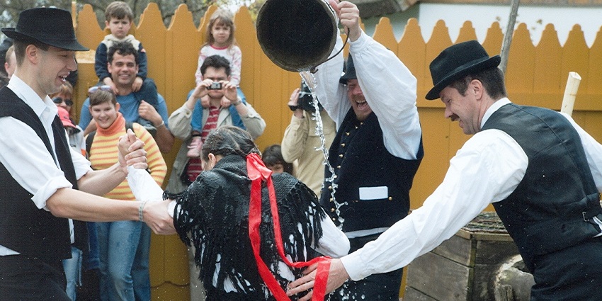 People in traditional Hungarian attire dancing and celebrating during the Hollókő Easter Festival in a historic village.