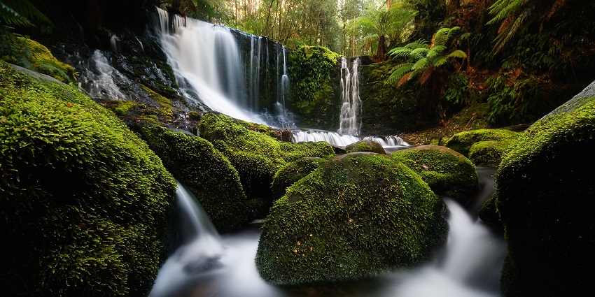 Columns of water falling over a curve-shaped landscape onto rocks covered in moss.