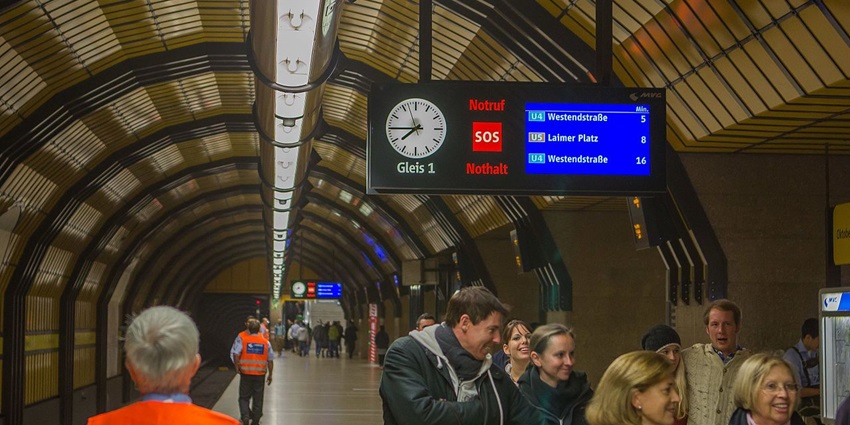 Theresienwiese station with people waiting on the platform under a board and staff