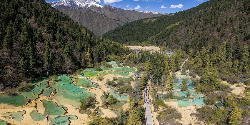 Aerial view of the Huanglong Valley and pools, showing dense forests and a snowy mountain