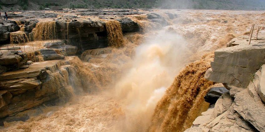 The golden-yellow water of Hukou Waterfall plunges powerfully through a narrow rocky channel.