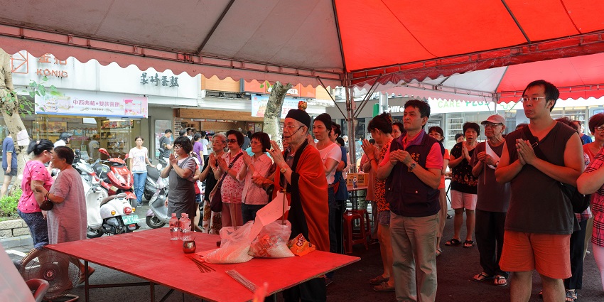 People standing and offering prayer in unison with folded hands inside a red tent