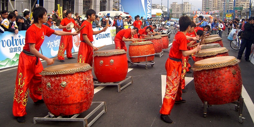 Performers in colourful attire with drums and flags for a cultural festival celebration.
