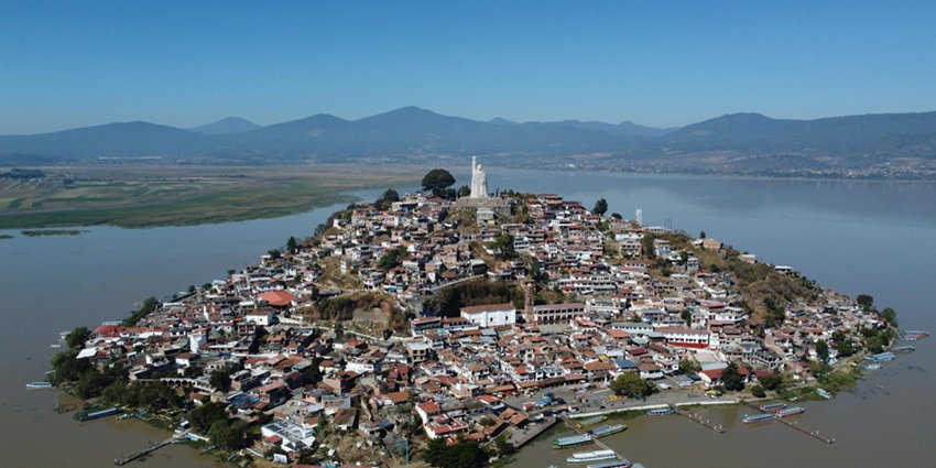 An image of the Janitzio Island rising from Lake Pátzcuaro with boats nearby.