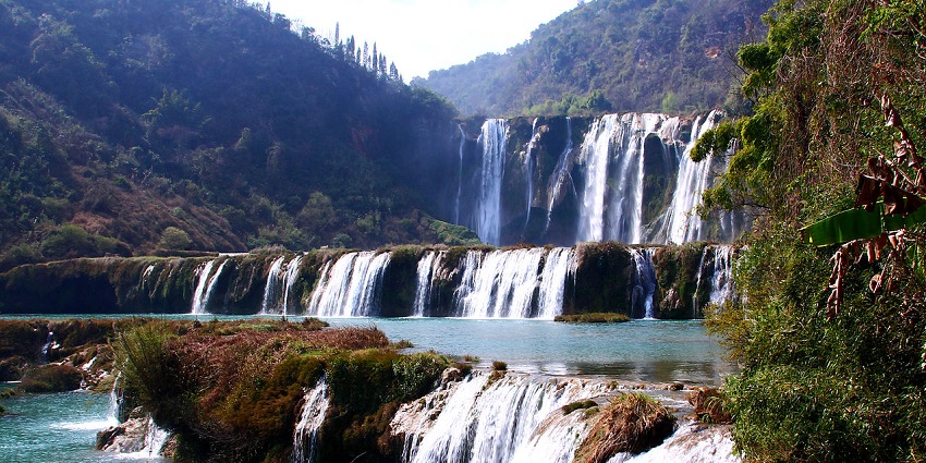 Jiulong Waterfall in China cascades dramatically in a dense green terraced landscape.