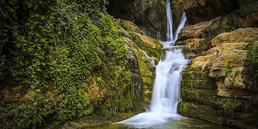 A stunning waterfall with whitish water cascading into a clear greenish natural pool below