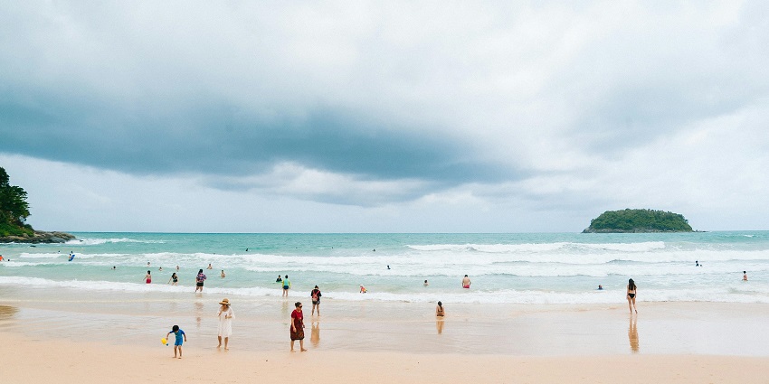 A view of Kata Beach in Phuket with clear water, white sand, and surrounding greenery.
