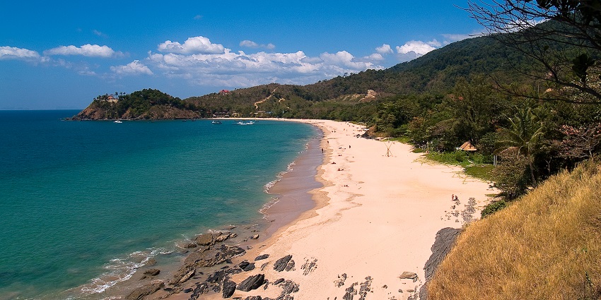 Golden beach at Koh Lanta with calm waves, a few tourists relaxing under soft evening light.