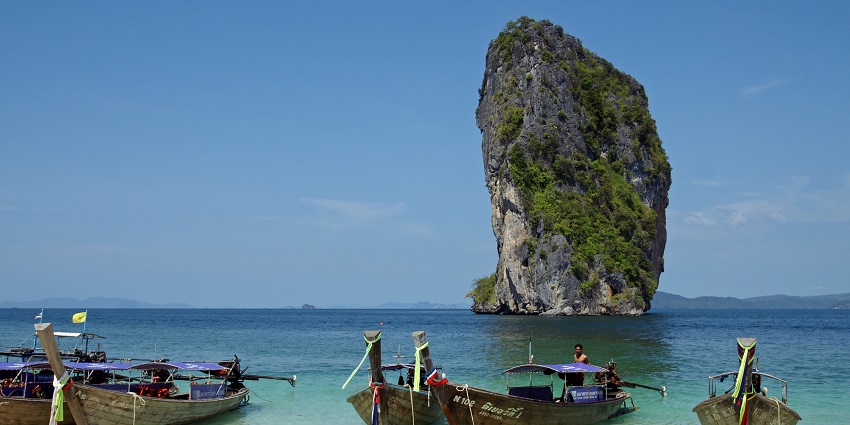 Serene white beach at places to visit near Krabi, Koh Poda, with a limestone cliff and boats.