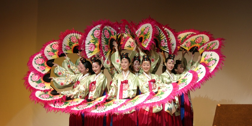 Korean dancers performing Buchaechum fan dance in vibrant hanbok with decorated fans during cultural festival celebration.