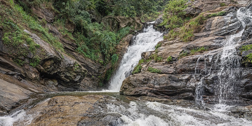 Milky white water thrusting down on rocks at Kuda Ravana Ella Waterfalls in Sri Lanka.