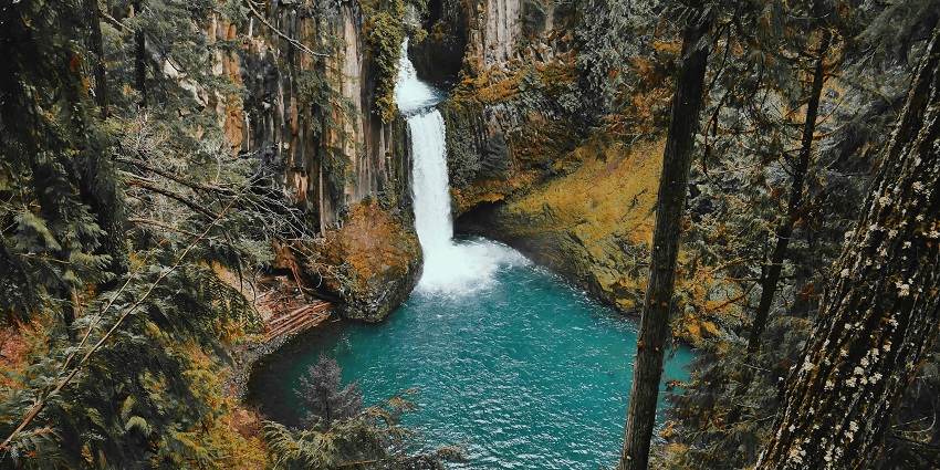 A turquoise pool cradles a waterfall, one of the hidden waterfalls in Zambia, surrounded by tall pines.
