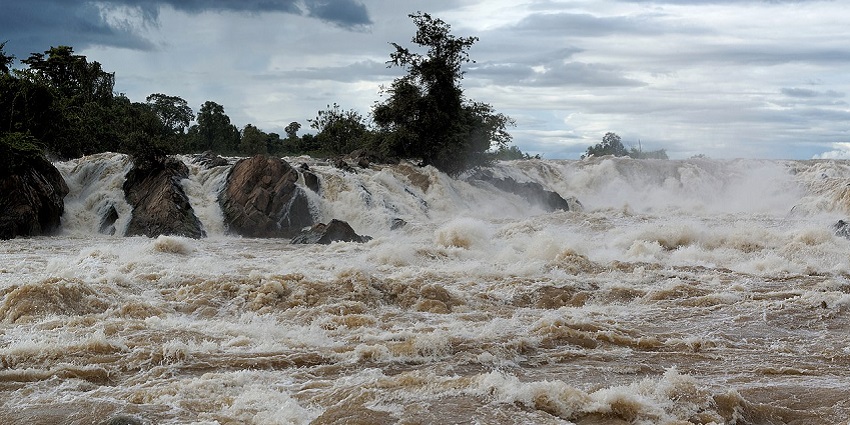 Waterfall with brown, fast-moving water flowing over rocks into a swirling pool below