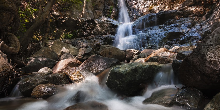 Waterfall cascading over stones, with sunlight shining on rocks and surrounding trees