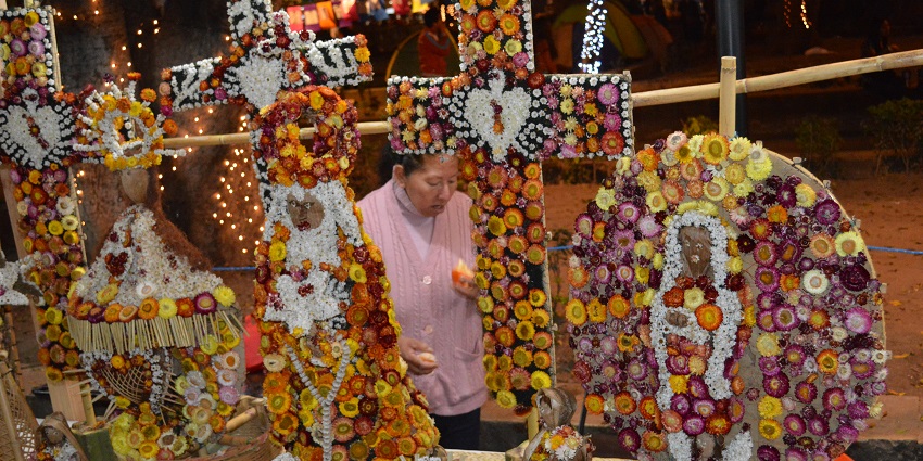A woman arranges intricate floral decorations shaped like crosses at a nighttime market.