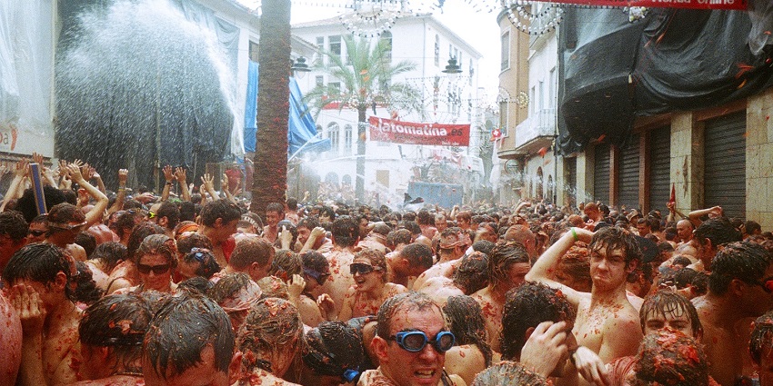 A crowd of people covered in tomato pulp celebrate the La Tomatina festival on a street.