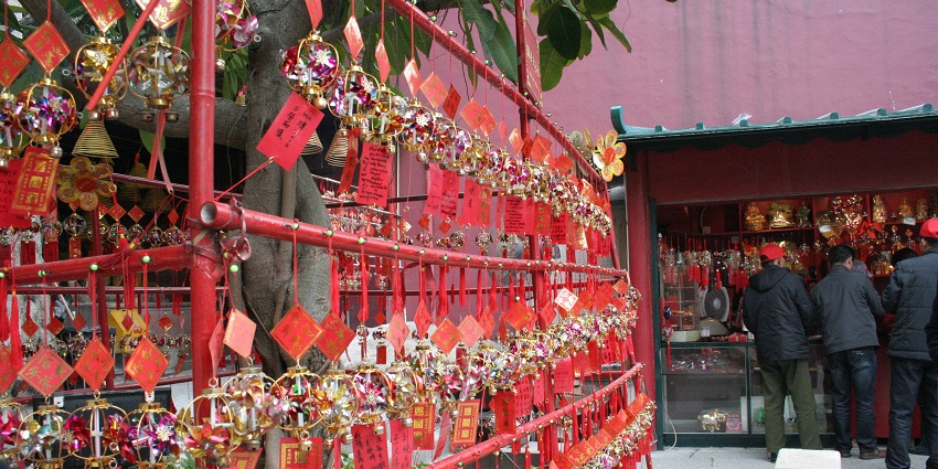 Red prayer cards hang in multiple rows on strings as devotees gather in the distance