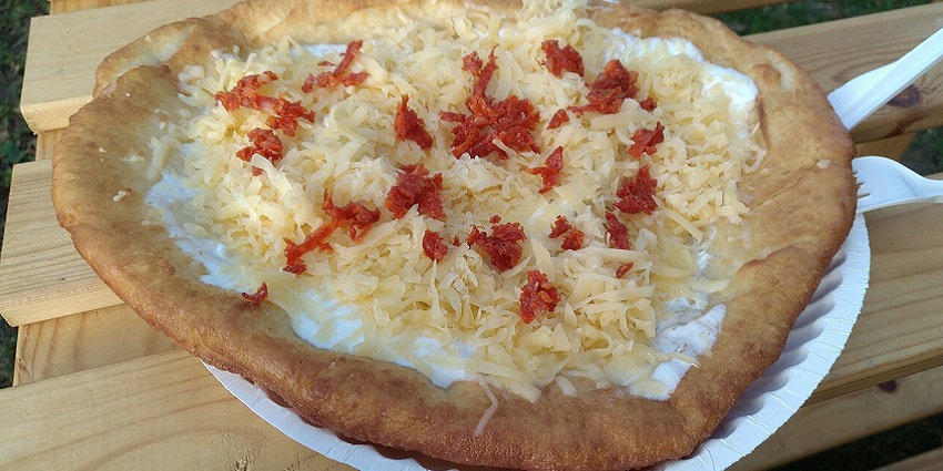 An image showing Lángos topped with sour cream and grated cheese, served hot.